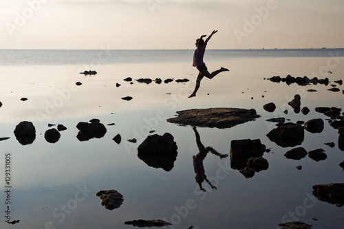 silhouette of a young girl soaring in a jump on the beach at sunrise with reflection in water photo