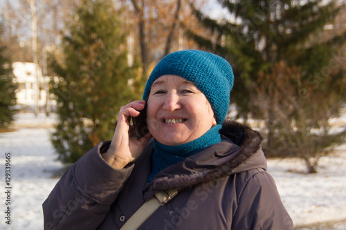 Portrait of mature woman talking on phone outdoor. Senior lady smiling and the in park at winter sunny day