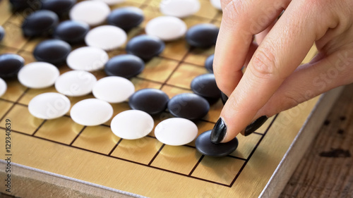 Close up view of female hand playing black and white stone pieces on Chinese go game board. Outside activity with natural sun light.