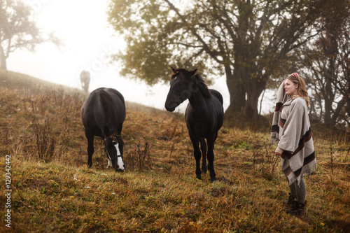 Woman with her horses. Concept about people and animals. Early morning. Misty mountain. Woman in boho style. © Serhii
