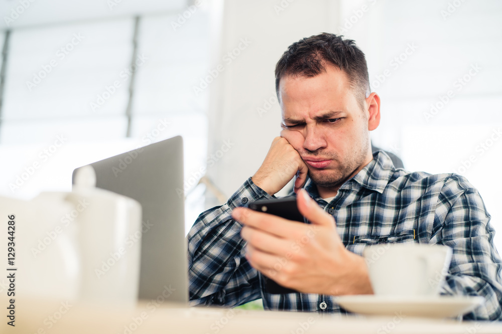 Tired handsome young freelancer is using a mobile phone while working at the coffee shop Tired handsome young freelancer is using a mobile phone while working at the coffee shop