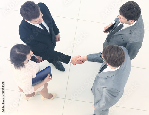 Business meeting. Top view of four people in formalwear standing close to each other while two of them handshaking