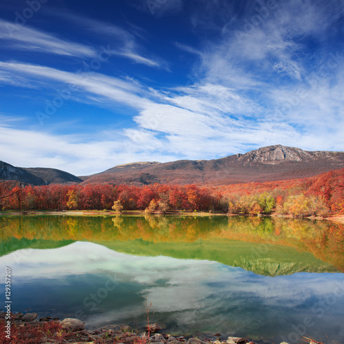 Scenic mountain lake with autumnal forest along the shore and bl