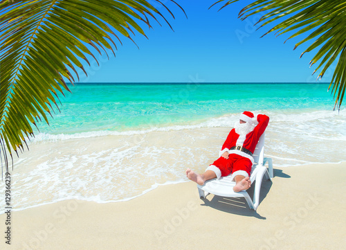 Christmas Santa Claus relax in sunlounger at ocean tropical sandy palm beach - Xmas and New Year's travel destinations to hot south countries concept