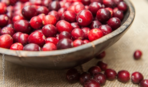 Fresh cranberries in rustic wooden bowl on burlap Background an