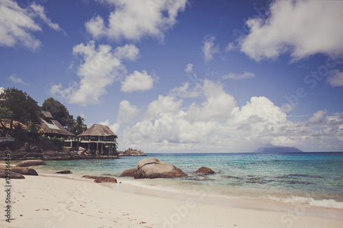 Beach of a tropical island with white sand and blue ocean on a hot Sunny day. Blue sky. On the shore a few small houses..