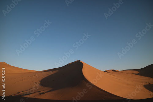 Deserto com grande duna em formato de pico em destaque  sombras projetadas na areia e c  u azul