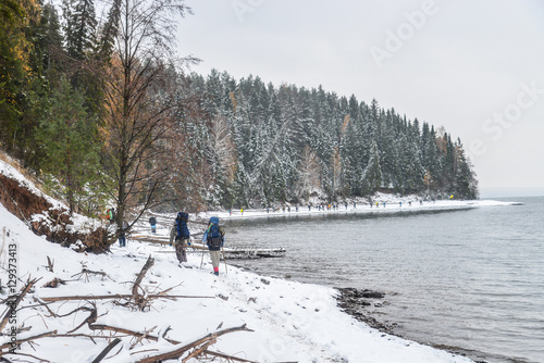 Large Group of people with backpack takes way on a snowy trail at riverside in winter