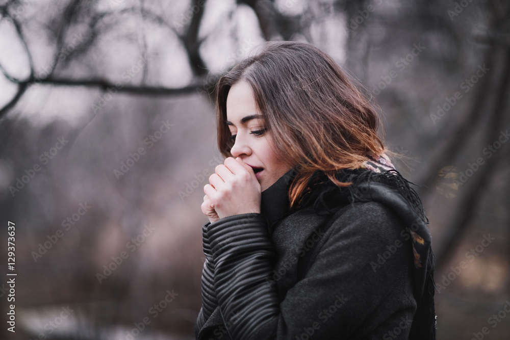 Attractive, charming young woman in a dark coat walking in the autumn park and warms frozen hands. Cloudy. Soft colors of nature. Attractive, charming young woman in a dark coat walking in the autumn park and warms frozen hands. Cloudy. Soft colors of nature.