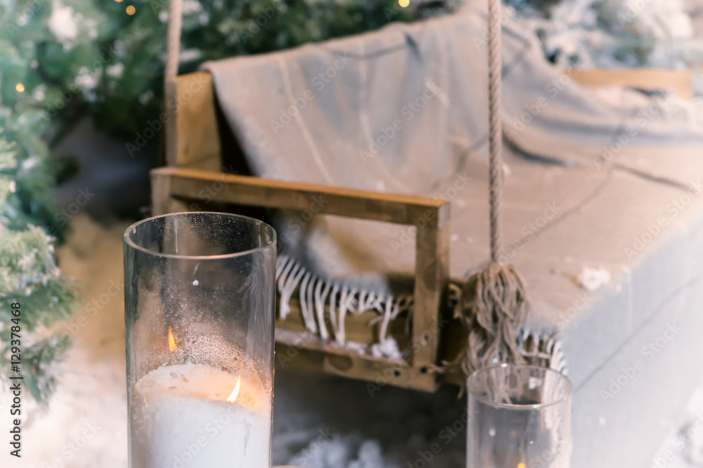 Close up of big candles in glass vases near swing in a snow-cove