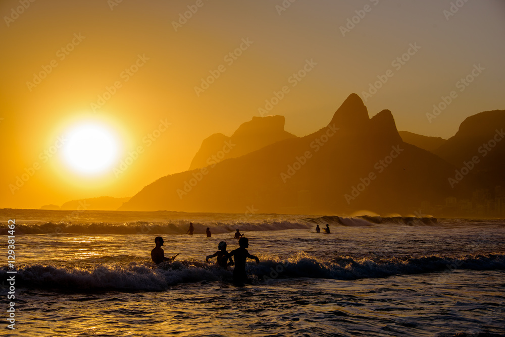 Unidentifiable silhouettes enjoying late afternoon sun rays on Ipanema beach in Rio de Janeiro, Brazil. Ipanema is one of the most expensive places to live in Rio.
