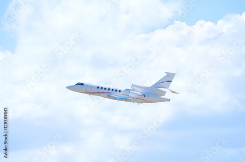A clean white private business jet airliner plane in flight climbing in altitude with beautiful fluffy clouds and blue sky in the background