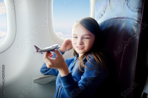 Adorable little girl traveling by an airplane. Child sitting by the window and playing with toy plane.