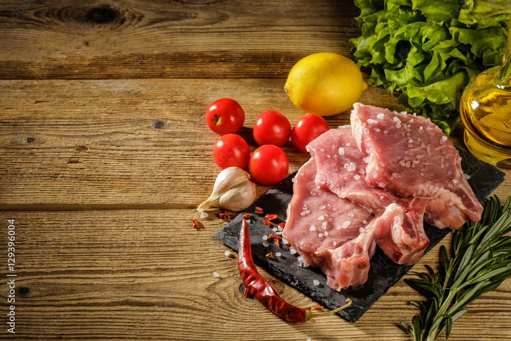 Raw pork steaks on stone board with herbs, tomatoes, garlic and Raw pork steaks on stone board with herbs, tomatoes, garlic and