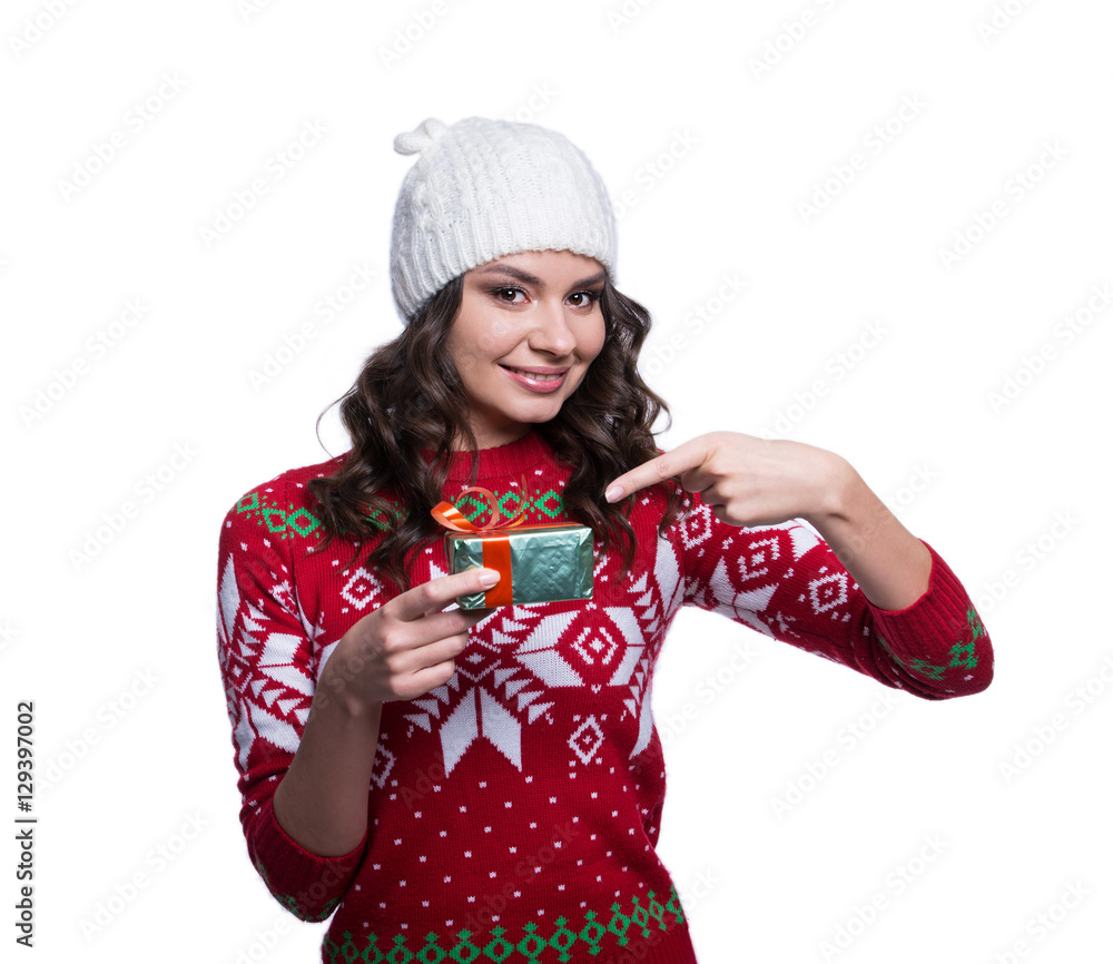 Smiling pretty sexy young woman wearing colorful knitted sweater with christmas ornament and hat, holding christmas gift. Isolated on white background. Winter clothes and christmas concept. Smiling pretty sexy young woman wearing colorful knitted sweater with christmas ornament and hat, holding christmas gift. Isolated on white background. Winter clothes and christmas concept.