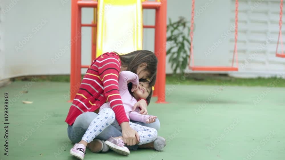 Young Asian mother hugging and kissing her little daughter at the park near the playground Young Asian mother hugging and kissing her little daughter at the park near the playground