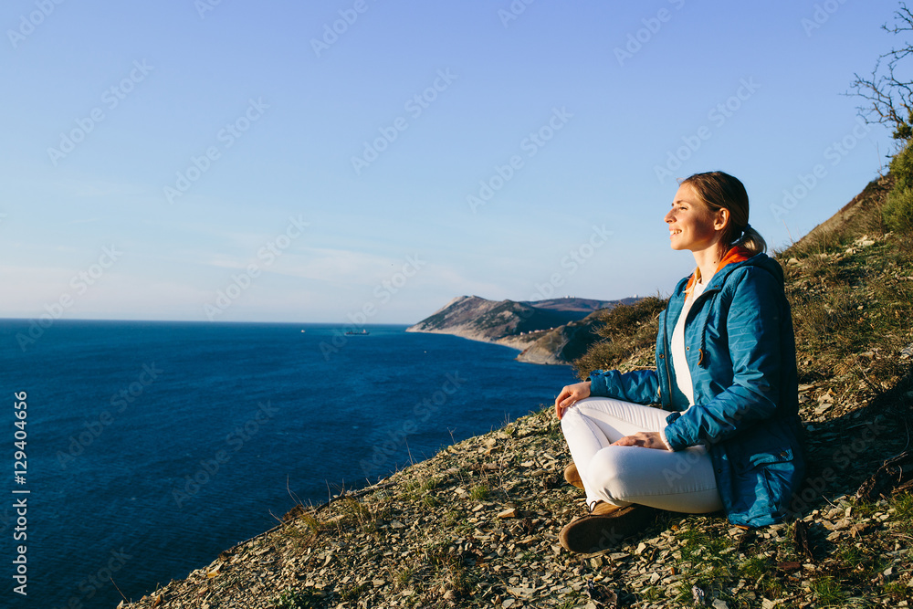 young woman traveler sitting on top of a cliff and looking at sea. Travel, Holidays, Freedom and Lifestyle Concept