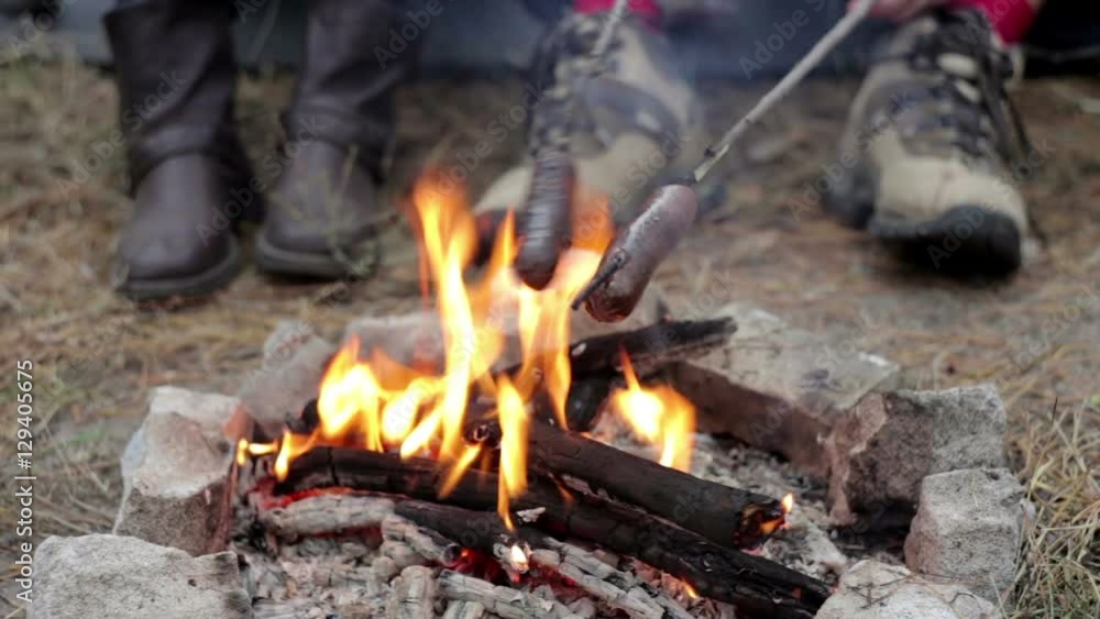 A Man with the Girl Cooking Sausages on Fire in the Forest A Man with the Girl Cooking Sausages on Fire in the Forest
