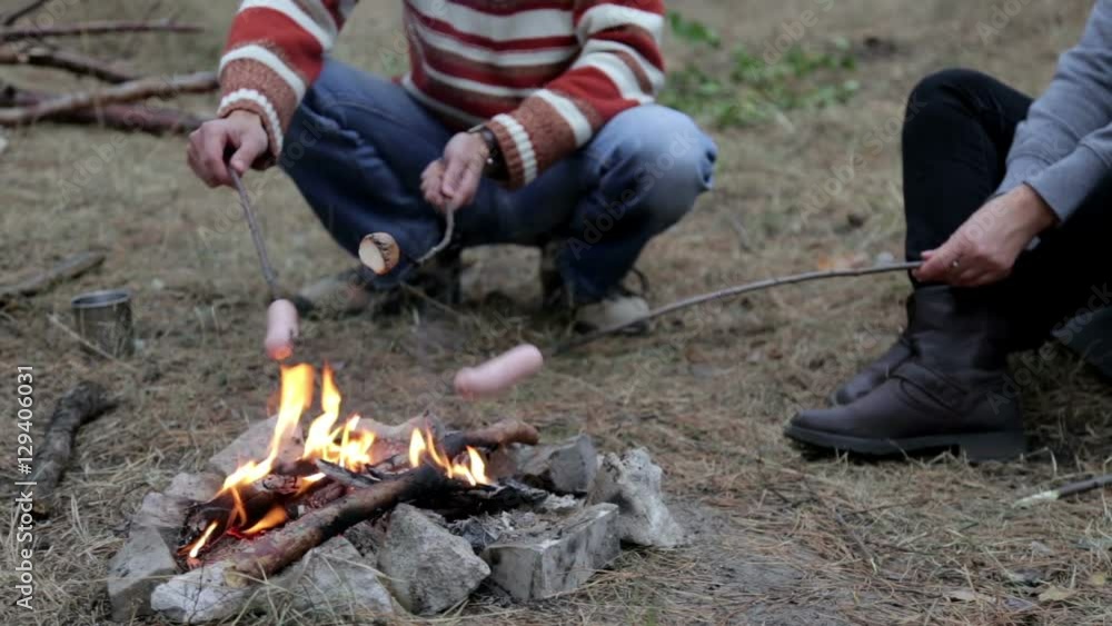 A Man with the Girl Cooking Sausages on Fire in the Forest A Man with the Girl Cooking Sausages on Fire in the Forest