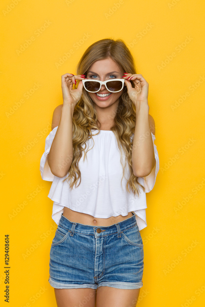 Fototapeta premium Smiling Woman In White Shirt And Shorts Posing With Sunglasses