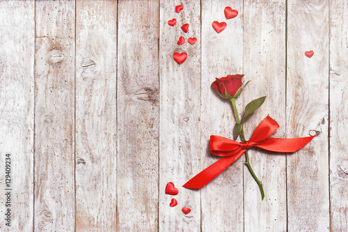 Beautiful red rose with ribbon and hearts on a wooden background