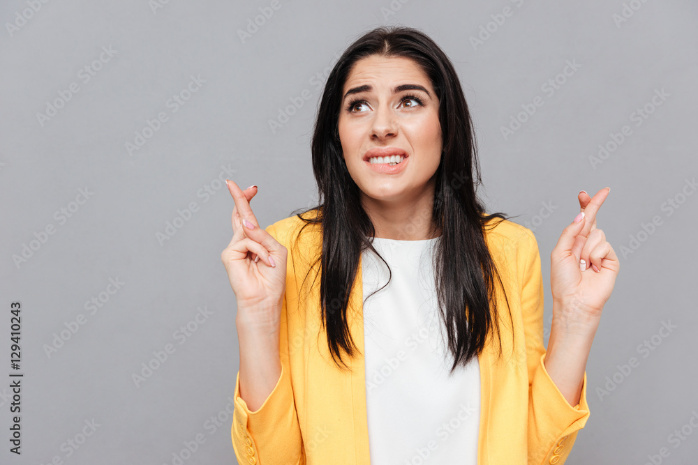 Confused young woman crossed fingers over grey background Confused young woman crossed fingers over grey background