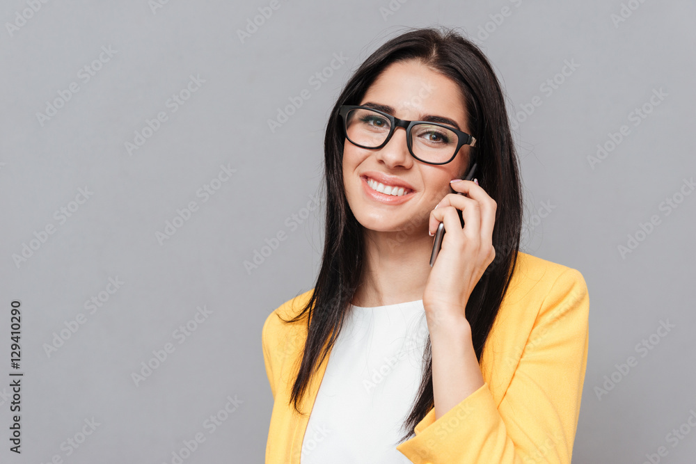 Cheerful woman talking by her phone over grey background Cheerful woman talking by her phone over grey background