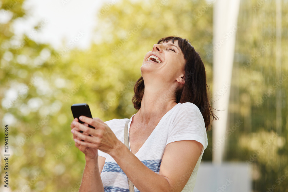 Laughing older woman holding smart phone outside