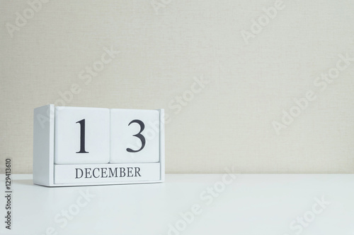 Closeup white wooden calendar with black 13 december word on blurred white wood desk and cream color wallpaper in room textured background with copy space , selective focus at the calendar