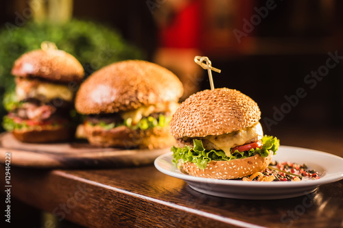 Three juicy tasty burger on the white plate on a dark background