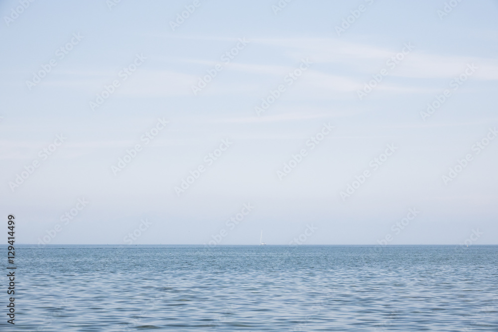Blue sea and sky with sail boat far away. Beautiful blue nature scene. Concept image of sailing alone and distance.
