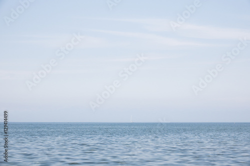 Blue sea and sky with sail boat far away. Beautiful blue nature scene. Concept image of sailing alone and distance.