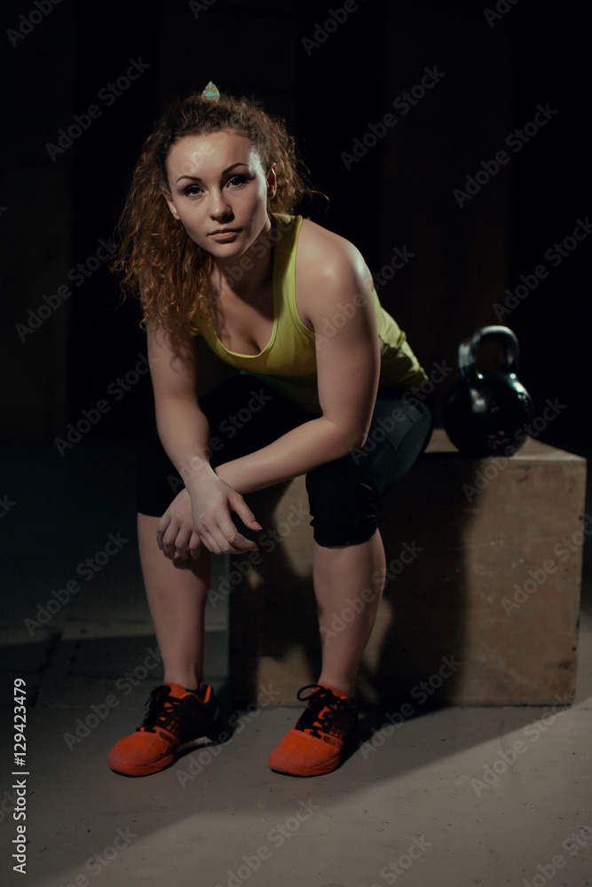 Young woman sits on a pedestal with weights at the gym Young woman sits on a pedestal with weights at the gym