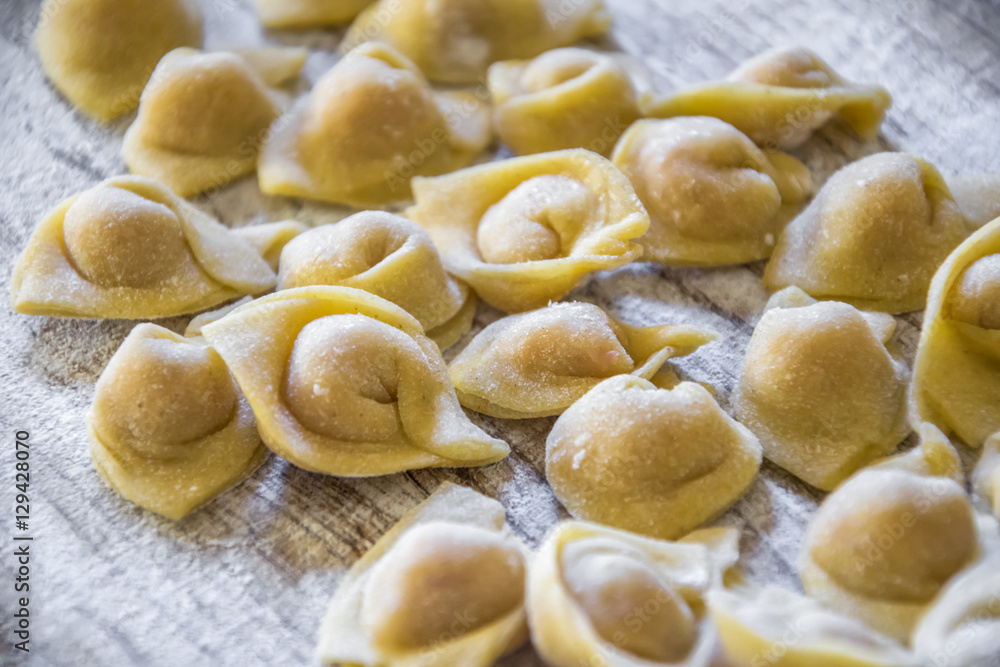  Raw italian cappelletti, fresh homemade pasta stuffed with cheese and meat on rustic wood table. Natural light.