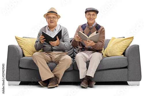 Two mature men with books sitting on a couch and looking at the camera