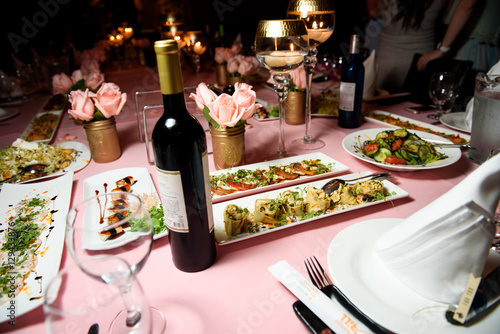 Bottle of wine stands among plates with snacks on pink tableclot photo