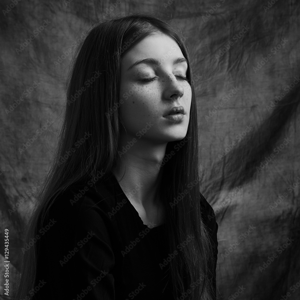 Dramatic black and white portrait of a beautiful lonely girl with freckles isolated on a dark background in studio shot Dramatic black and white portrait of a beautiful lonely girl with freckles isolated on a dark background in studio shot