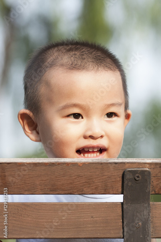 Cute Chinese baby boy playing on a bench in a park