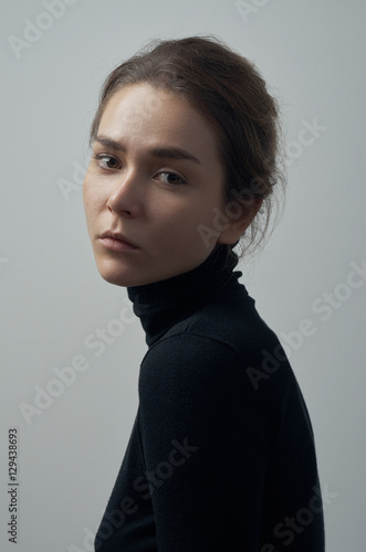 Dramatic portrait of a young beautiful girl with freckles in a black turtleneck on white background in studio