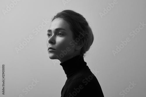 Dramatic black and white portrait of young beautiful girl with freckles in a black turtleneck on white background in studio © Parad St