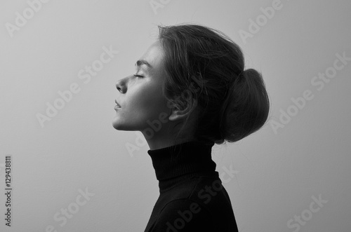 Dramatic black and white portrait of young beautiful girl with freckles in a black turtleneck on white background in studio