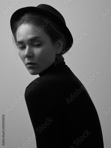 Dramatic black and white portrait of young beautiful girl with freckles in a black turtleneck and a hat on a white background in studio