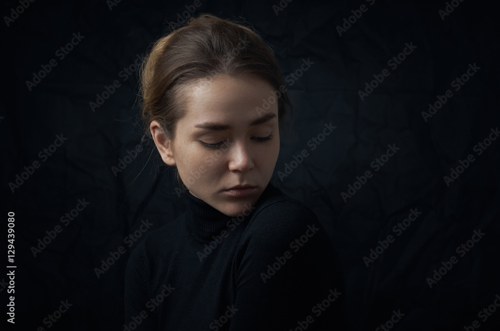 Dramatic portrait of a young beautiful girl with freckles in a black turtleneck on black background in studio Dramatic portrait of a young beautiful girl with freckles in a black turtleneck on black background in studio