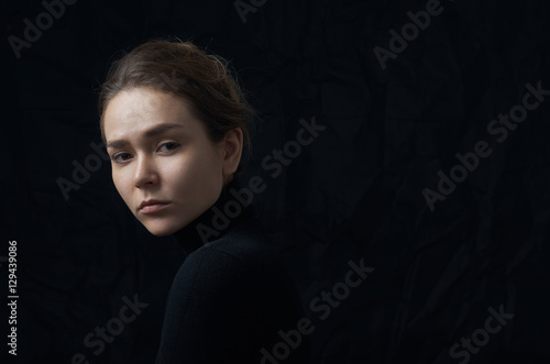 Dramatic portrait of a young beautiful girl with freckles in a black turtleneck on black background in studio