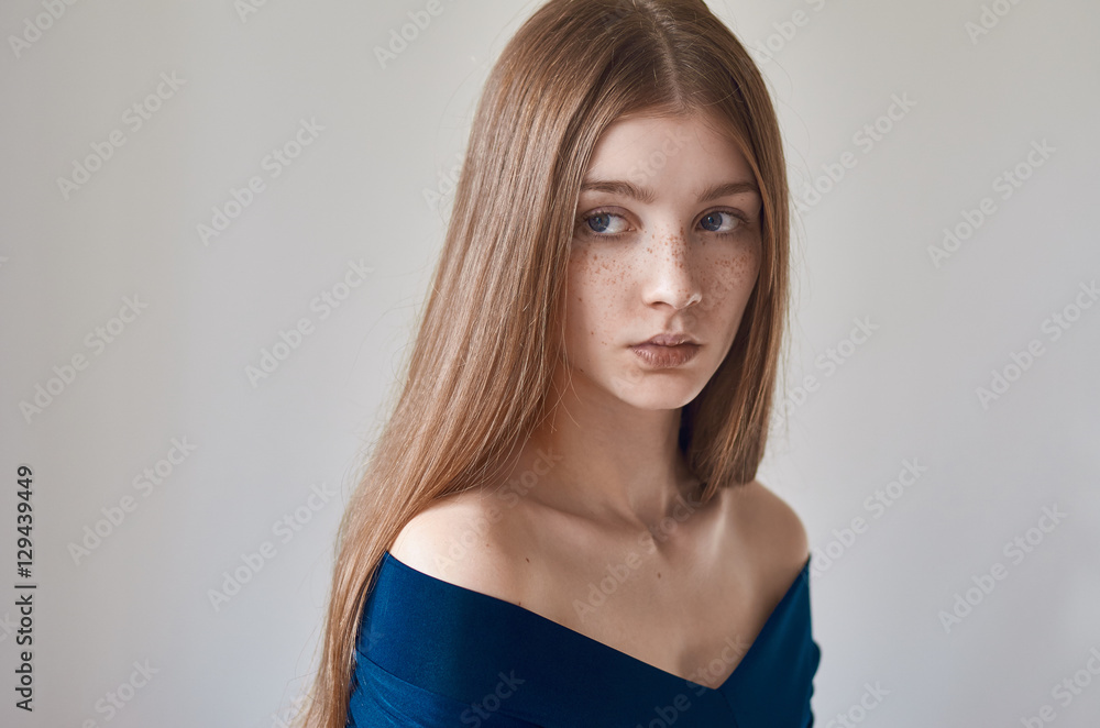 Beauty theme: portrait of a beautiful young girl with freckles on her face and wearing a blue dress on a white background in studio Beauty theme: portrait of a beautiful young girl with freckles on her face and wearing a blue dress on a white background in studio