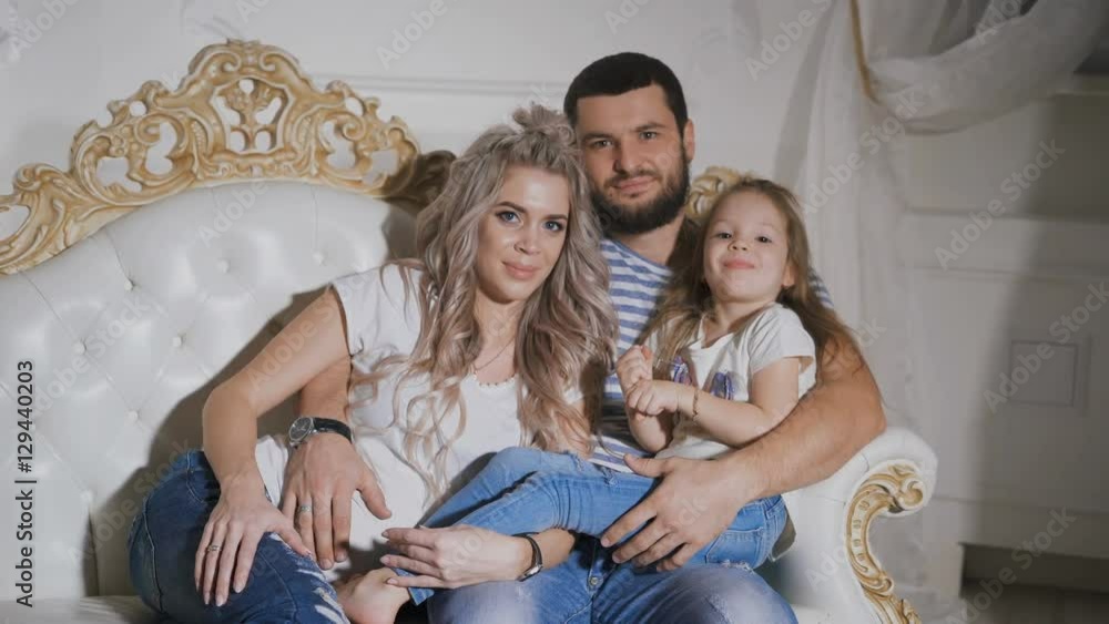 Close-up of happy family expecting new baby together on the sofa. Father, pregnant mother and little daughter are sitting together on the sofa hugging each other. Close-up of happy family expecting new baby together on the sofa. Father, pregnant mother and little daughter are sitting together on the sofa hugging each other.