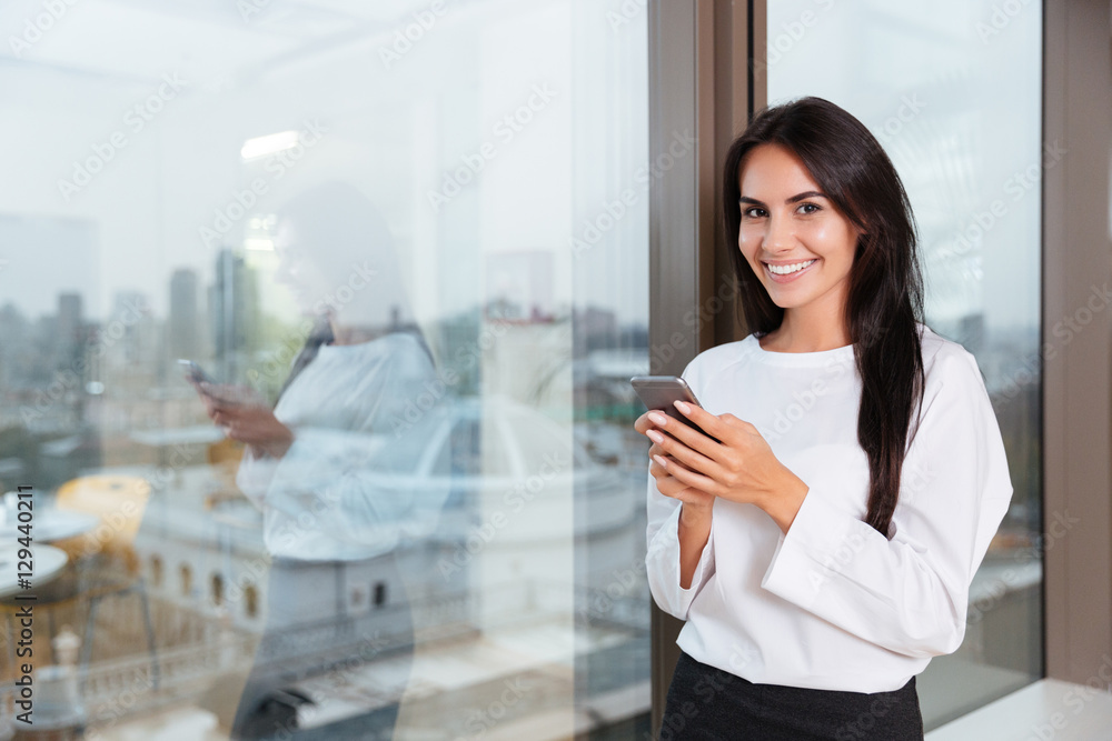 Smiling businesswoman using smartphone near the window in office