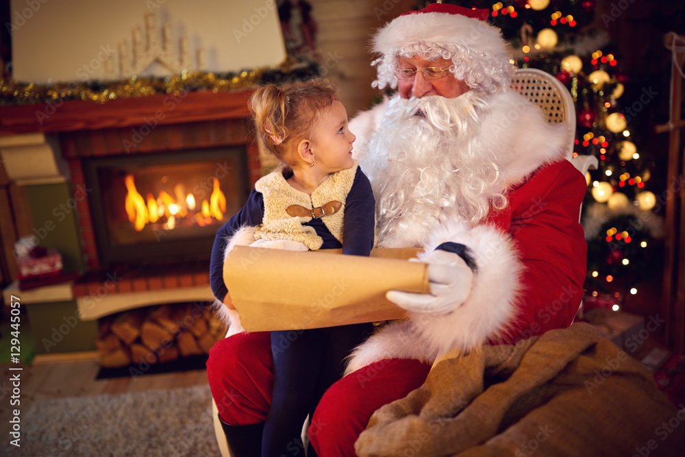 Obraz premium Sweet girl and Santa Claus choosing her present from list.
