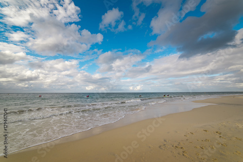 The Indian Ocean laps gently onto the white sandy shore of beautiful beach near Busselton, South Western Australia protected by Geographe Bay on a blue sky and white cloud afternoon in early summer.