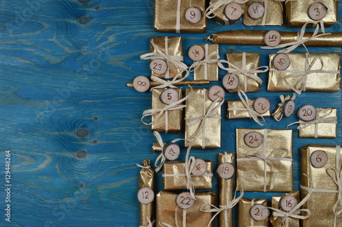 Border of advent calendar with twenty four golden presents on teal wood with negative space to the left